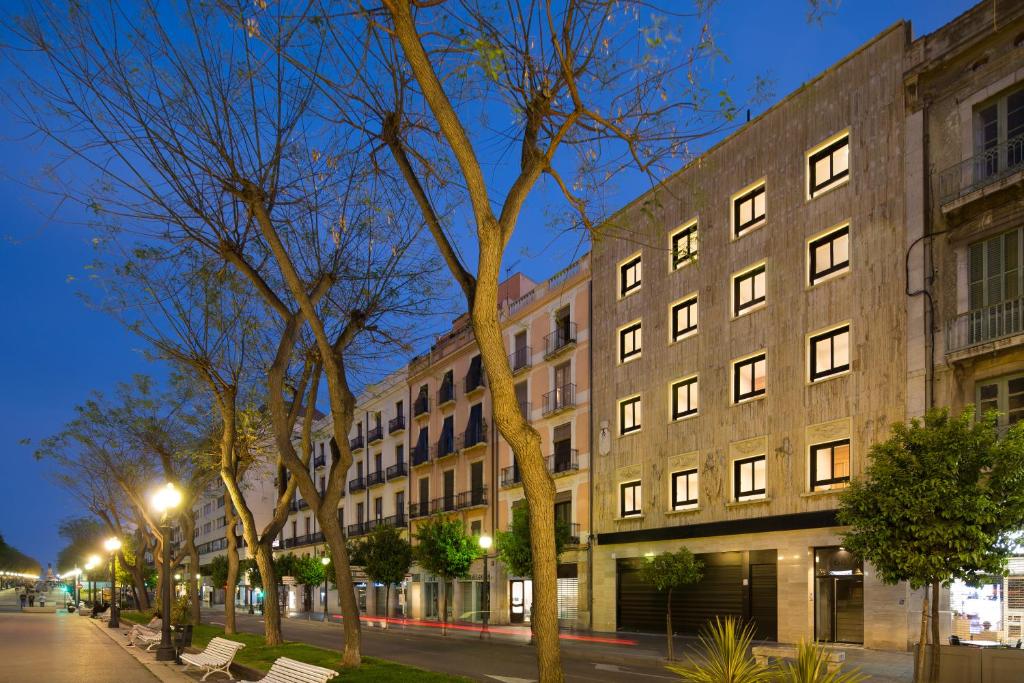 Exterior de TGNA Rambla 68 de nit, amb vistes a la Rambla Nova, una de les zones més emblemàtiques de Tarragona. La ubicació de l'edifici ofereix als hostes un accés fàcil als principals atractius turístics, botigues i zones d'oci, fent-lo perfecte per a turistes, professionals i famílies que busquen allotjament còmode al centre de la ciutat.