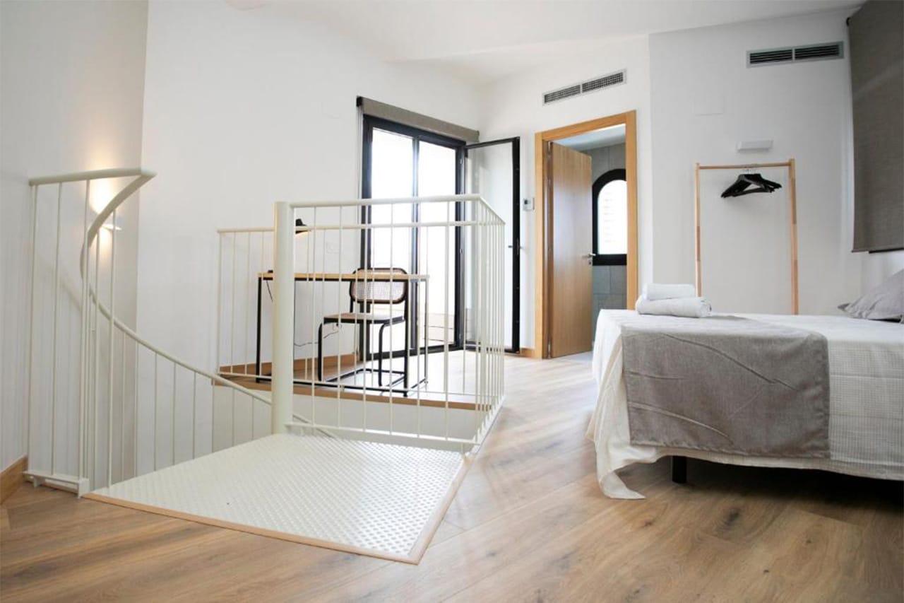 Foto de l'interior d'un àtic dúplex de TGNA Reding 22, amb un llit de matrimoni i accés directe a la terrassa exterior. Un espai ampli i còmode per a 4 persones, ideal per gaudir de la ciutat i descansar amb total comoditat.