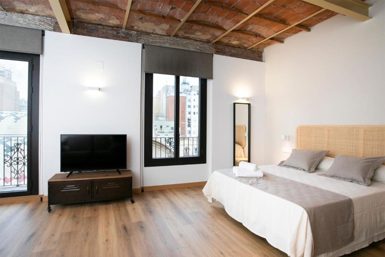 Foto d'un apartament amb llit de matrimoni i balcó amb vistes a la Plaça Corsini i al Mercat Central de Tarragona, situat a TGNA Reding 22. Espai ideal per a parelles o viatgers que volen gaudir de la ciutat amb comoditat i vista privilegiada.