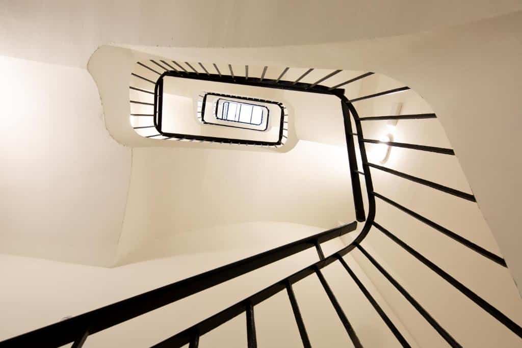 Detall de l'escalinata interior de TGNA Rambla 68, amb vista al sostre, mostrant els diferents trams d'escala que connecten els pisos de l'edifici. Aquesta imatge destaca l'arquitectura moderna de l'edifici, ideal per a aquells que busquen un allotjament amb disseny contemporani i bones connexions interiors. Perfecte per a famílies, professionals i turistes que volen allotjar-se al centre de Tarragona.