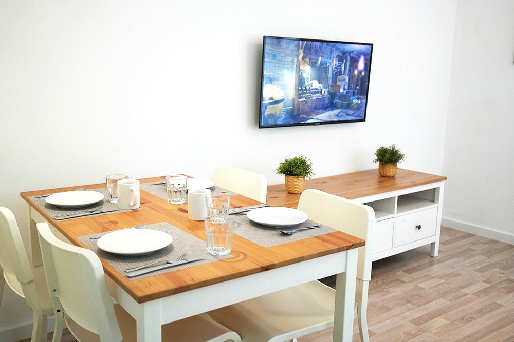 Menjador de TGNA Llúria 11, un apartament turístic modern situat a Tarragona, capital de la Costa Daurada. El menjador compta amb una taula per a quatre persones, ideal per a families, parelles i grups de turistes. Amb molta llum natural, és un espai perfecte per dinar, treballar o relaxar-se després d'un dia explorant la ciutat. L'apartament està a prop de la Rambla Nova i ofereix fàcil accés als llocs d'interès turístic i les platges de Tarragona.