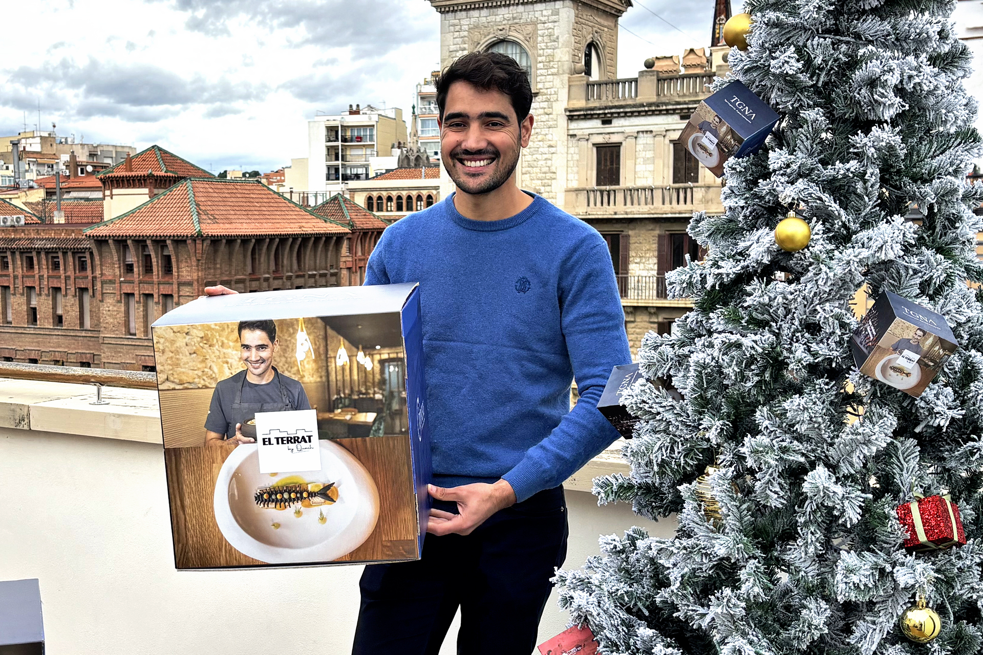 Chef Moha Quach mostrant la caixa amb la imatge del restaurant El Terrat, un sopar per a dues persones inclòs al sorteig de Nadal i Cap d’Any 2025-2026 de TGNA Tarragona Apartaments.